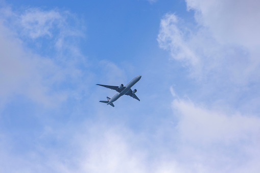 View of flying plane high in sky against backdrop of white clouds.