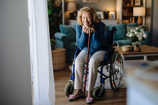 Portrait of senior woman in wheelchair resting hands on walking stick