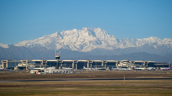 Varese, Italy. The MXP Milan Malpensa international airport. View of the airport from the gates side. Airplanes at the gates. Mountain in the background
