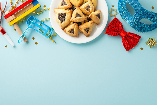 Snapshot of Purim joy: Top view triangular pastries, Star of David figures, and merry-making items like confetti, mask, noisemakers, all laid out on serene blue background, space reserved for words