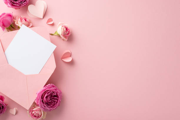 istock 8 March greetings setup. Top view of partially open envelope, emotional message card, slender paper hearts, youthful rose blossoms positioned on light pink backdrop, with space for your text or advert 2020640632