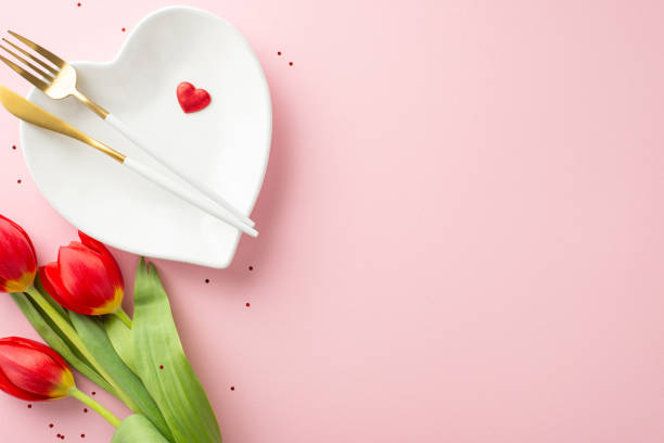 istock Charming 8 March celebration setting. Overhead photo of dinner scene, heart-formed plate, premium cutlery, sequins, love symbols, bouquet of tulips on gentle pink background, with space for wording 2020640639
