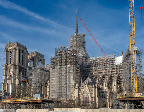 Paris, France - 02 15 2024: Notre Dame de Paris. Panoramic view of the renovation site with scaffolding and the spire topped with the golden rooster of Notre-Dame cathedral from the quays