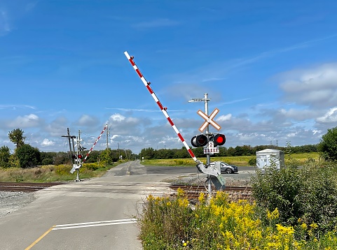 clarington, canada - september 07 2023: a railroad crossing with arms flashing lights at a track where a train is going to pass by