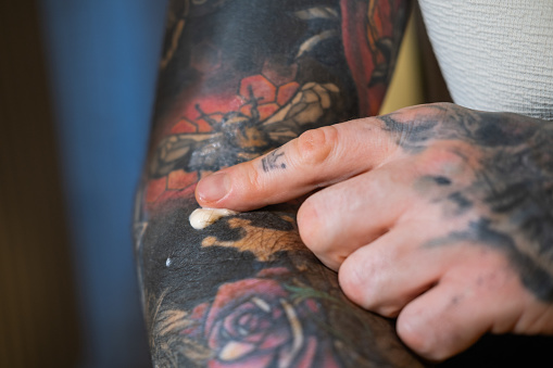 A man applies cream to his tattoo.