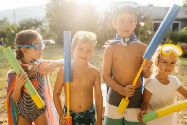 Group of children posing with squirt guns and prepare to have some fun in the yard with water fight on a hot summer day