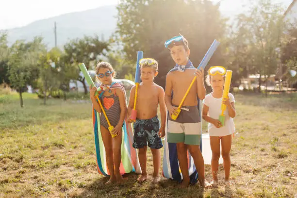 Group of children posing with squirt guns and prepare to have some fun in the yard with water fight on a hot summer day