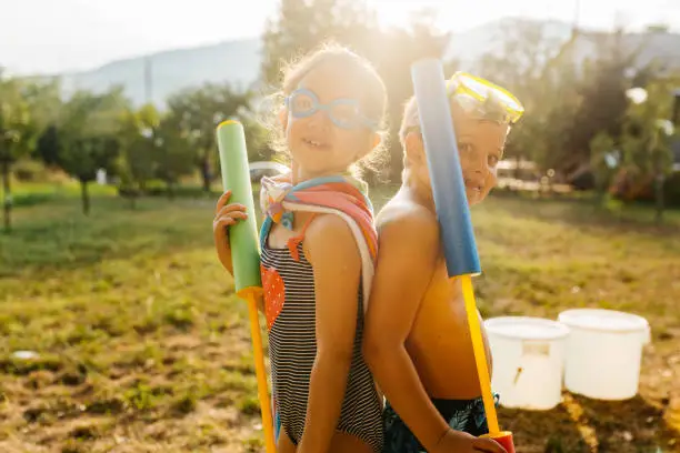 Group of children posing with squirt guns and prepare to have some fun in the yard with water fight on a hot summer day