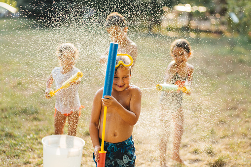 Children having fun spraying with water guns and enjoy refreshing on a hot summer day