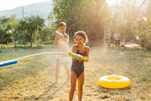 Children having fun spraying with water guns and enjoy refreshing on a hot summer day