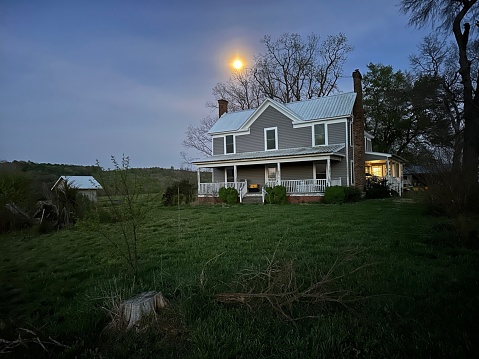 A full moon rising above a grey farmhouse with a white roof. Shot in Coleridge, North Carolina, USA