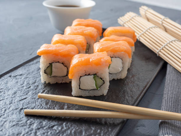 istock Philadelphia sushi rolls on a black textured plate stand on a gray background. There are bamboo chopsticks nearby. Side view, Japanese cuisine 2020739964