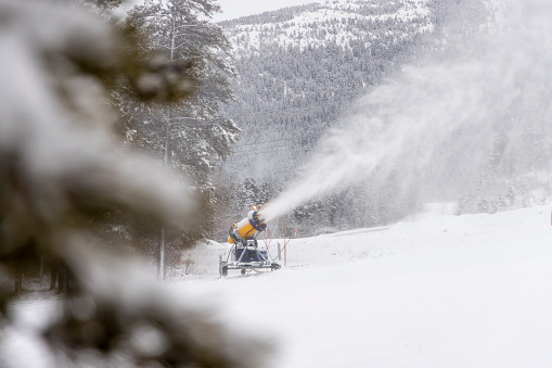 Snow makers make snow on ski hill with snowy forest and snowcapped mountains behind, Powder Keg Ski Hill