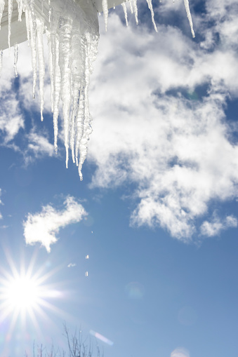 Icicles hang off eavestrough in sunlight and lofty clouds in sky