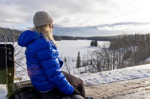 Mature woman sits on back of truck and looks across frozen lake to mountains