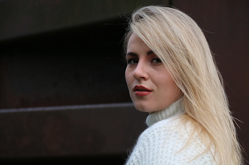 A headshot of a Ukrainian model looking over her shoulder. She is wearing long, blond straight hair, makeup, and a white turtleneck sweater.