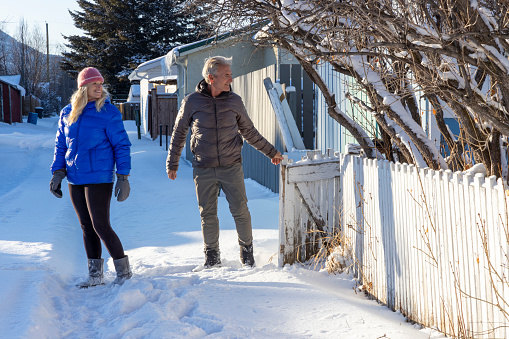 Mature couple walk down snowy lane behind house