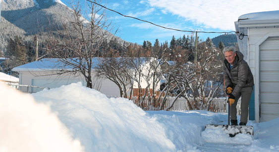 Mature couple lean against vehicle in winter and look towards foothills and mountains covered in snow