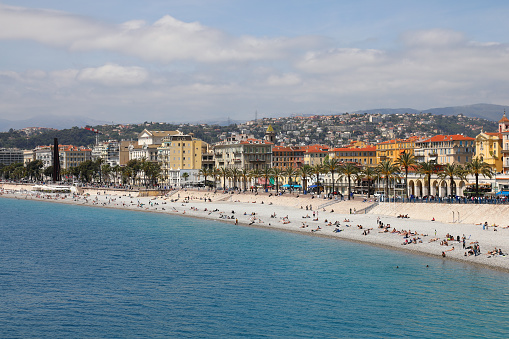 Nice, France - April 28, 2023: A beach along the shore of the Mediterranean Sea and along the buildings of the city. In the distance, people on the beach are enjoying the charm of the sea and the view.