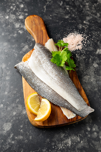 Fresh sea bass fillets on wooden board with herbs.