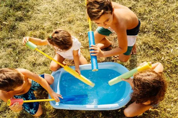 Children filling up squirt guns , prepare for water fight on a hot summer day in the yard