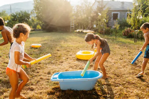 Children filling up squirt guns , prepare for water fight on a hot summer day in the yard