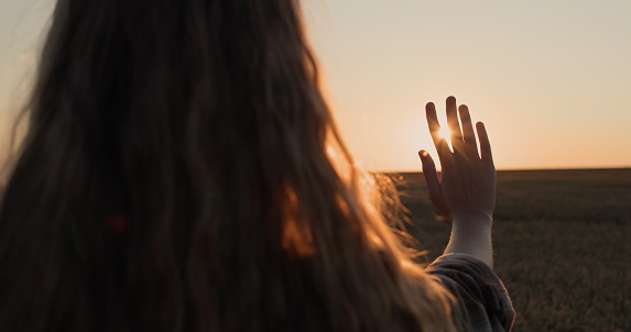 Una chica con un hermoso cabello largo extiende su mano hacia el sol poniente. photo
