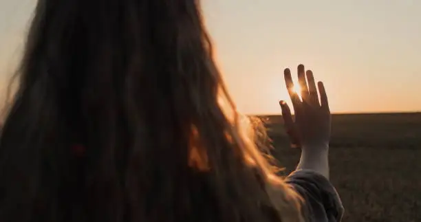 A girl with beautiful long hair holds out her hand to the setting sun