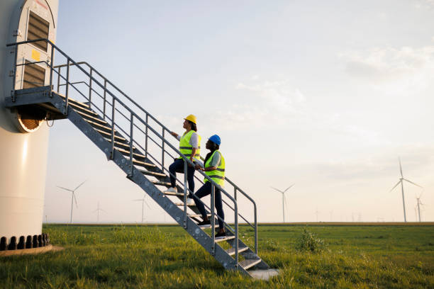 istock Two Female Engineer wearing uniform ,helmet hold document inspection work in wind turbine farms rotation to generate electricity energy. 2020824039