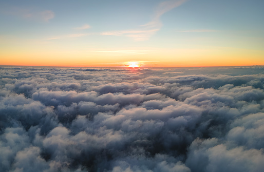 Aerial view from airplane window at high altitude of dense puffy cumulus clouds flying in evening.