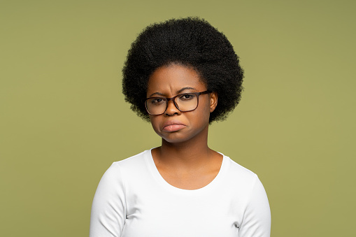 Displeased upset african american female with frowning face expression because of being discontent, disappointed. Unhappy grumpy black woman in contrasting white clothing isolated on studio background