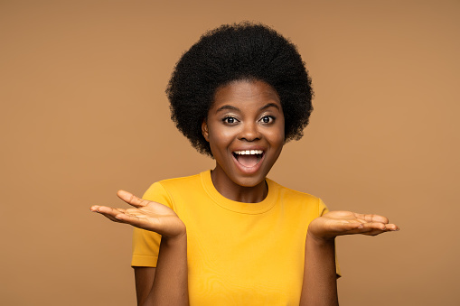 Happy glad cheerful smiling dark skinned woman with curly hairstyle, unusual white teeth, expression of joy and happiness on face, looking at camera, posing for picture, holding palms opened isolated.