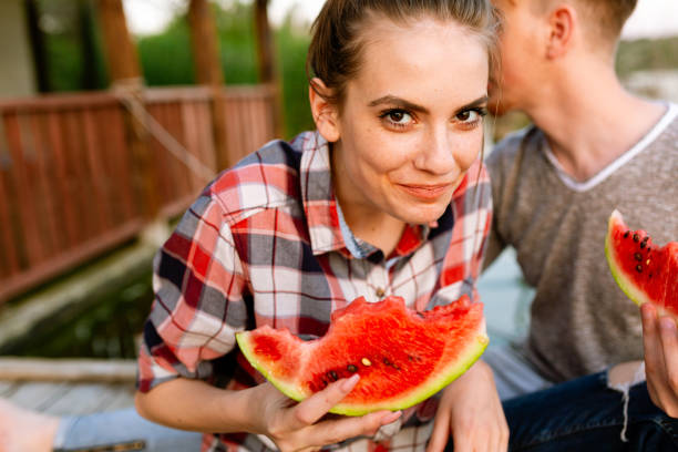 Young couple sitting by the lake and eating watermelon
