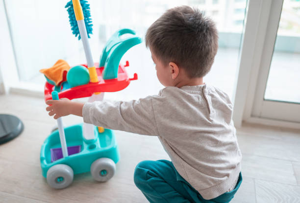 A cheerful two-and-a-half-year-old boy finds joy in playing with his cleaning set toy, mimicking chore activities with enthusiasm and innocence. Encourage early learning and responsibility with this heartwarming image of a little helper in action. Chore role playing showcasing his playful yet responsible nature while dressed in cozy clothing, bringing a sense of warmth and cleanliness to the home