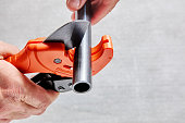 Cutting plastic pipe with ratchet cutter in shape of scissors, plumbers hand holds tool.