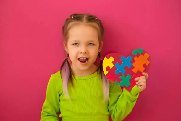 Photo of Girl talks about autism by showing heart-card decorated with puzzles