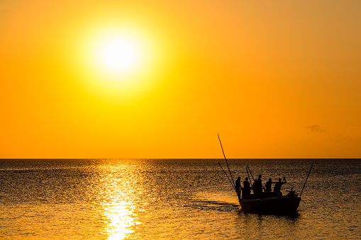 Silhouettes of fishermen in boat against sunset. Zanzibar, Tanzania