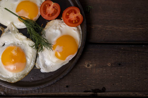 istock Fried eggs in a pan with vegetables and herbs on a black background. 2021063813