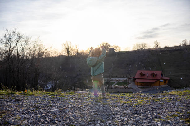 a little girl is watching the sunset with her arms raised