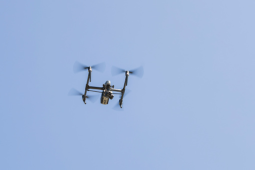 Aerial filming drone in action, silhouetted against blue sky.
