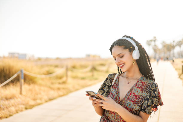istock Young latin american woman using her mobile phone while walking on the beach on a sunny summer day. 2021109602