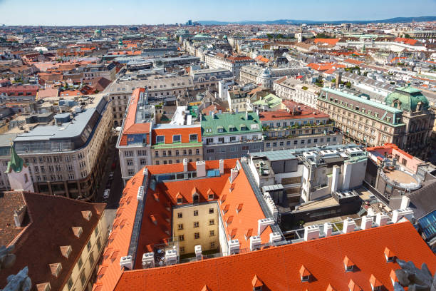 A wide clear daytime view of Vienna’s skyline, showcasing a mix of historic rooftops and modern buildings under a bright blue summer sky. Perfect for themes of travel, cityscapes, and urban life.