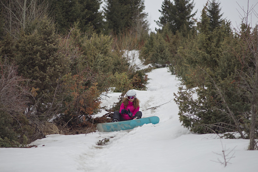 Young woman sitting on snow and adjusting her snowboard