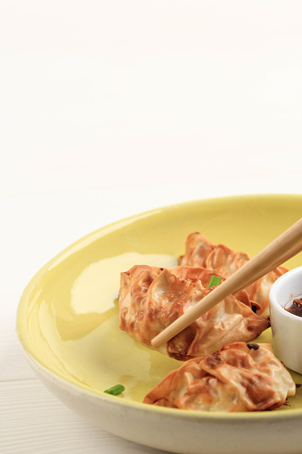 Gyoza Asian Potstickers with Sauces Served in Yelloe Ceramic Plate with Chopsticks and Spring Onion over White Wooden Background. Airfryer Cooking with no Oil.