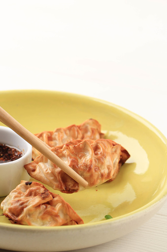 Gyoza Asian Potstickers with Sauces Served in Yelloe Ceramic Plate with Chopsticks and Spring Onion over White Wooden Background. Airfryer Cooking with no Oil.