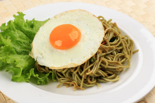 close up spicy healthy green instant fried noodle with shiny sunny side egg and lettuce on white ceramic round plate. - editorial front view sunlight light effect ストックフォトと画像