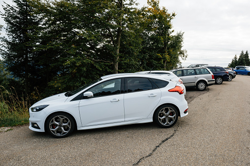 Mummelsee, Germany - Sep 22, 2018: Side view at the white sport Ford hatchback car parked on empty parked near hiking road in the Black Forest - tilt-shift lens used