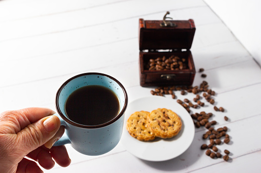 Woman's hand drinking a cup of coffee with homemade cookie and coffee beans in the background.
