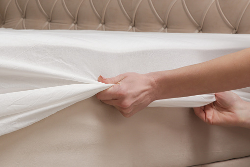 Changing bed sheets. Woman is putting on a fitted white cotton sheet on a mattress while making the bed.