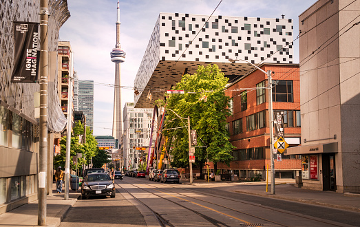 Toronto, Canada - 06 05 2021: Sunny summer day view along McCaul Street in downtown Toonto with fascinating modern OCAD University building in foreground and CN Tower in background.